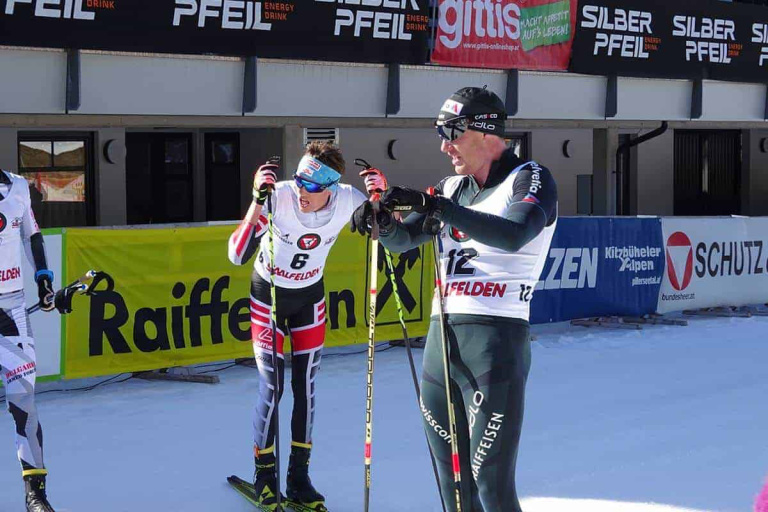 Langläufer in Saalfelden warten auf den Start in sportlicher Atmosphäre mit Werbebanner.