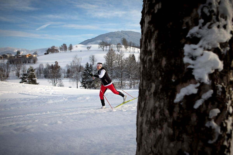 Langläufer in der verschneiten Landschaft Saalfeldens, umgeben von Bäumen und Hügeln.