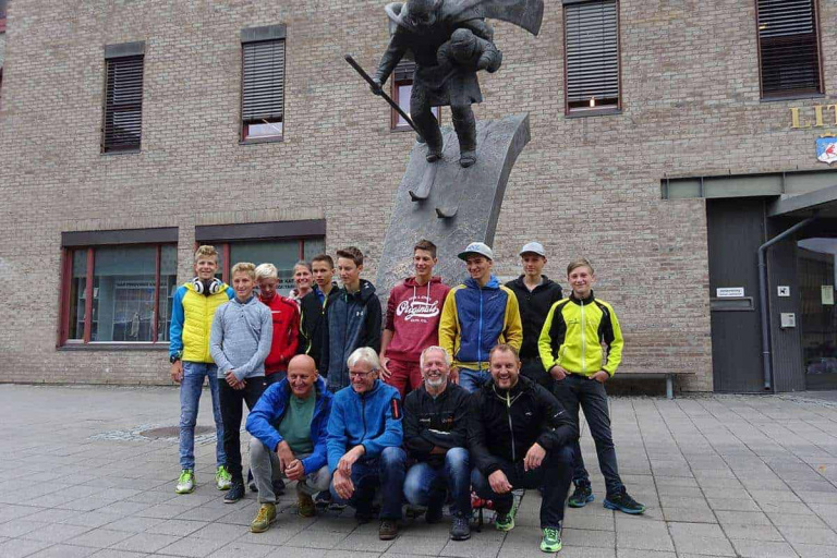 Gruppe junger Langläufer und Trainer vor einer Skulptur in Saalfelden.