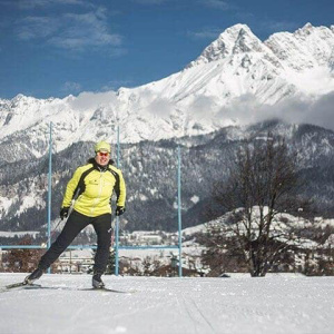 Langläuferin in gelber Jacke vor schneebedeckten Bergen, ideal für Langlaufkurse.