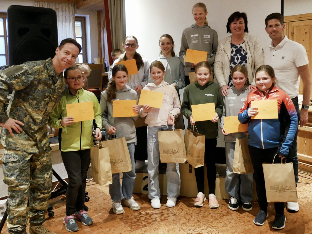 Gruppe mit Kindern und zwei Erwachsenen bei einer Siegerehrung mit Urkunden und Papiertaschen in einem Innenraum